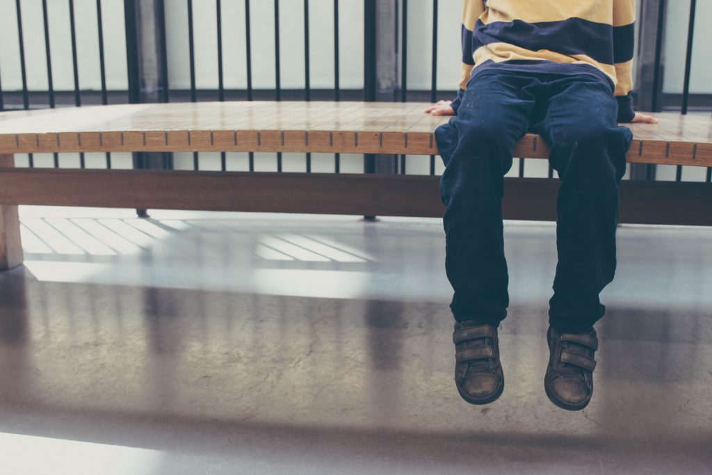 Foto de Michał Parzuchowski en Unsplash donde se observa los pies de un niño sentado en solitario